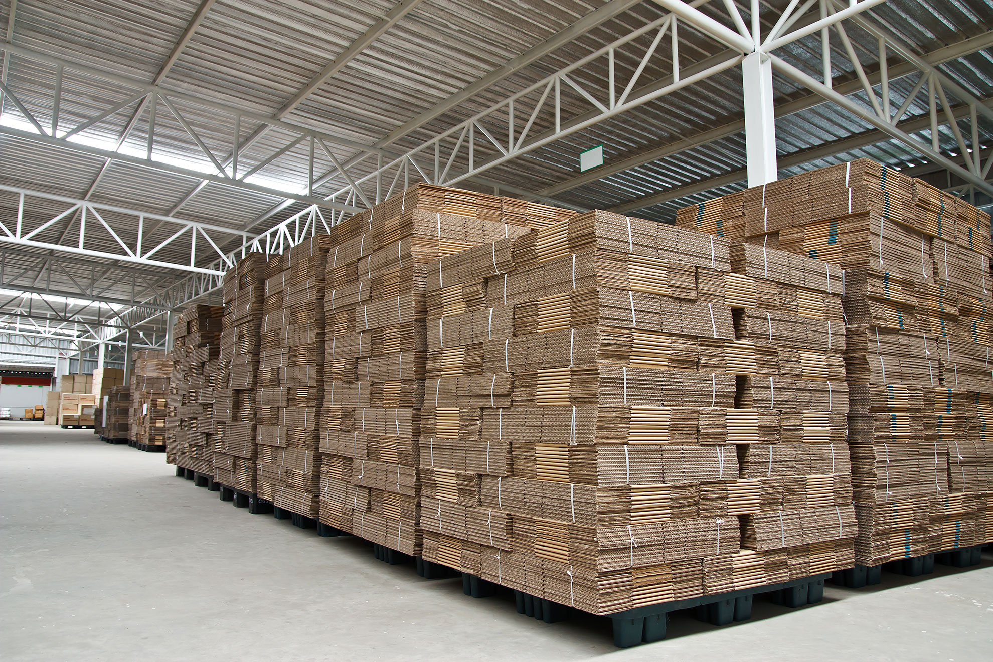 Stacks of cardboard sheets in a warehouse, representing packaging paper production and logistics.