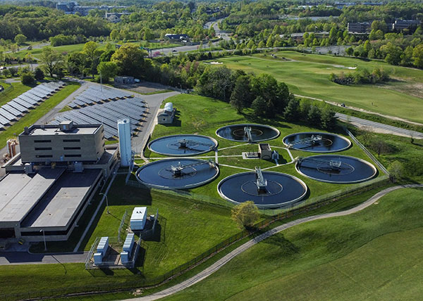 Aerial view of a wastewater treatment plant with circular clarifier basins and surrounding green landscape.